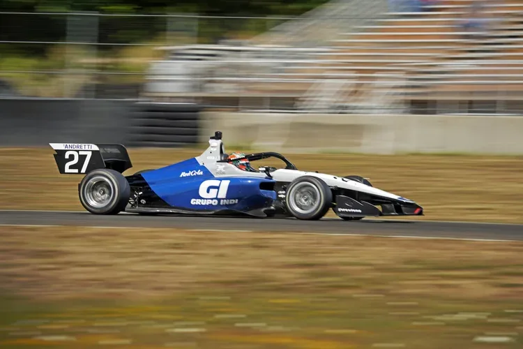 A Formula racing car with the number 27 and logos from Grupo Indi and Red Cola speeding on a racetrack, with a blurred background indicating motion.