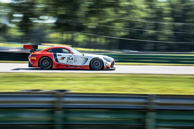 A red and white race car moving at high speed on a road with a blurred background of trees and clouds.