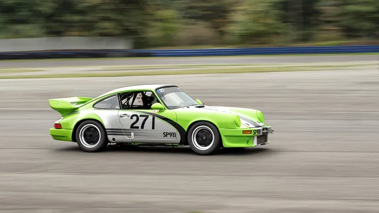 A bright green and silver race car with the number 27 on its door, driving on a racetrack with a blurred background.