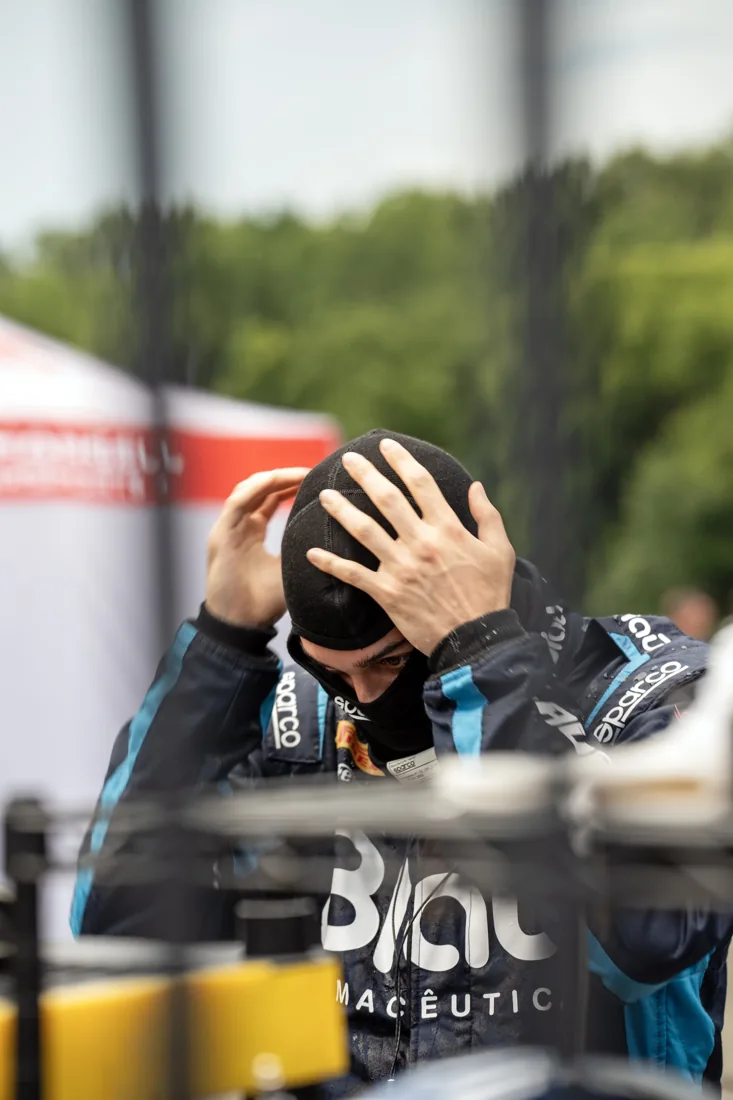 Race car driver adjusting his helmet before a race with a blurred background of trees.