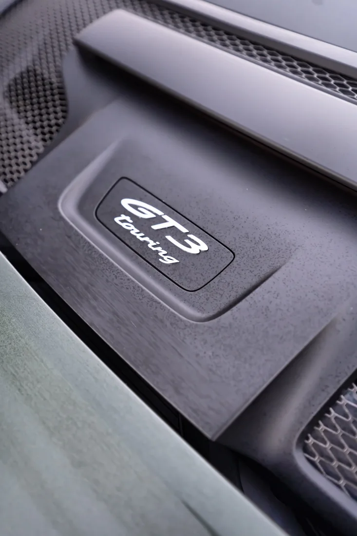 Close-up photo of a GT3 Touring badge on a car, with carbon fiber accents and metallic trim.