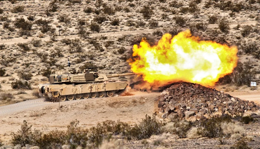 Tank gunnery exercise with a bright fireball in desert terrain
