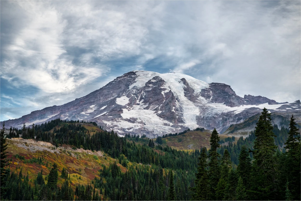 Mount Rainier above autumn forest beneath dramatic clouds